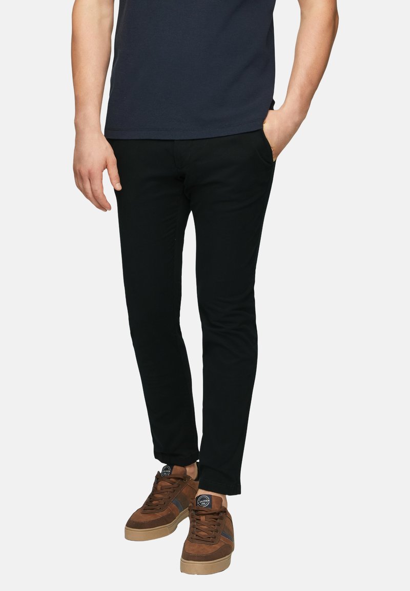 Czarne, dopasowane spodnie o gładkiej fakturze, z przednimi kieszeniami. Noszone z brązowymi zamszowymi trampkami i granatowym t-shirtem.