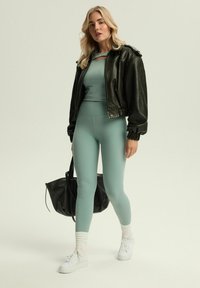 Sportowy strój z miętową crop topą i legginsami z wysokim stanem, połączony z czarną skórzaną kurtką bomberką i czarną torbą typu tote.