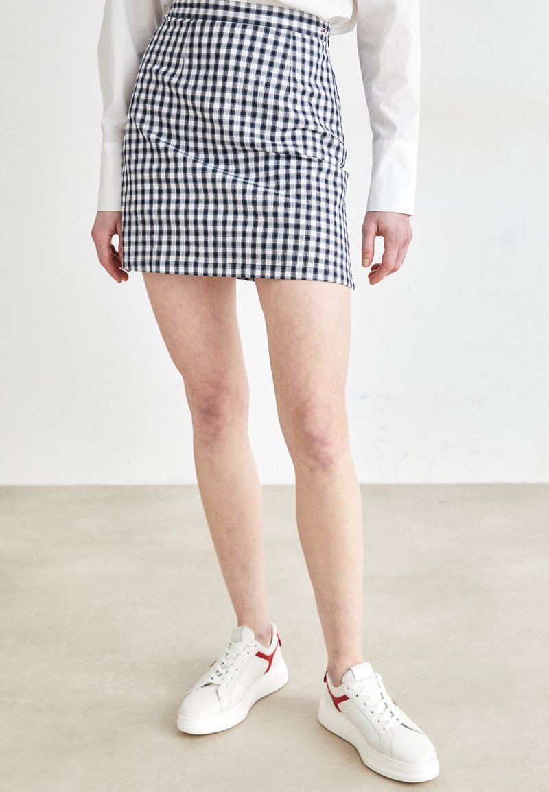 Navy- und weiße Gingham-Minirock, taillierter Schnitt mit hoher Taille, kombiniert mit weißen Sneakern mit roten Akzenten.