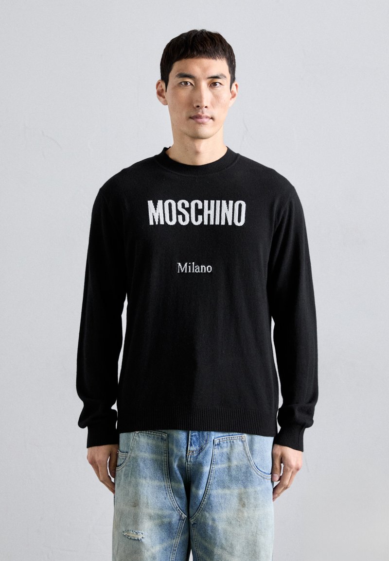 Schwarzer Strickpullover mit dem Schriftzug "MOSCHINO" und "Milano" in Weiß. Langärmlig, mit gerippten Bündchen und Saum, kombiniert mit ausgebleichten blauen Jeans.