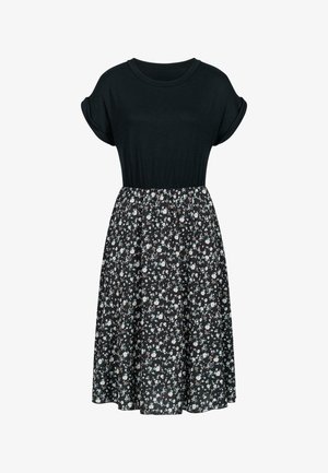 Melna T-kreklu kleita ar īsām sarullētām piedurknēm, pieguļošu augšu un platu, līdz ceļgaliem garu svārku, kas rotāta ar mazu ziedu rakstu uz tumša fona.