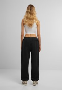 Schwarze Sweatpants aus weichem Material mit entspannter Passform. Mit einem elastischen Bund und einer Gesäßtasche ausgestattet. Tragen Sie sie mit einem weißen Cropped-Top.