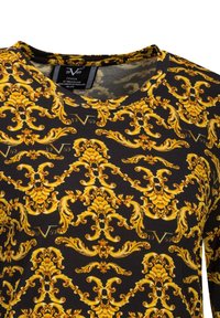 Langarm-Oberteil aus schwarzem Stoff mit einem auffälligen, goldfarbenen Barockmuster, rundem Ausschnitt, weicher Textur und Etiketten mit Marken- und Herkunftshinweisen.