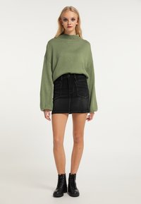Strik grøn sweater med høj krave, parret med en sort denim miniskirt. Sorte snørebodsstøvler fuldender outfittet.