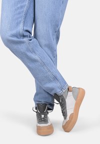 Graue und weiße Sneakers mit sandfarbenen Akzenten, strukturierten Sohlen und grauen Schnürsenkeln, kombiniert mit hellblauen Jeans.