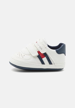 White toddler sneaker with a rounded toe, velcro straps, navy accents, and red and navy stripes. Made of synthetic materials, textured surface.