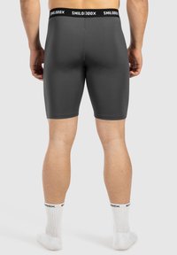 Grå kompressionsshorts med en tætsiddende design, prydet med et sort talje bælte med "SMILODON" branding. Båret med hvide sokker.