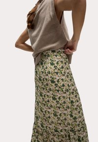 Un pull sans manches beige en tricot associé à une jupe fluide à motif floral verte et beige, avec un ourlet volé.