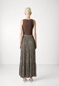 Smeđa kratka majica s dugim, slojevitim suknjom s leopard uzorkom. Model nosi prozirne cipele s blok petom. Glatka tekstura, opušteni kroj.