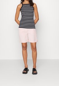 Top sin mangas a rayas blancas y negras combinado con pantalones cortos de color rosa claro. Sandalias negras tipo slip-on, los pantalones cortos tienen puños enrollados y una textura suave.