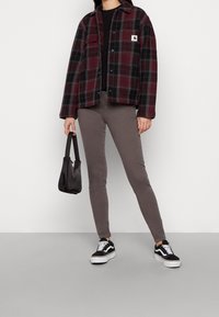 Chaqueta de franela a cuadros negra y roja, pantalones gris ajustados, zapatillas negras con acentos blancos y un bolso pequeño negro.