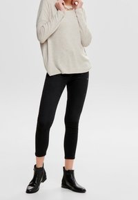Pull en maille beige clair, associé à un jean skinny noir et des bottines noires. Le pull a une coupe décontractée et un col rond.