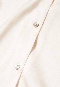 Tissu couleur crème avec deux boutons ronds translucides cousus sur la patte d'une chemise ou d'un chemisier.