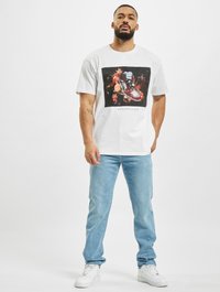 T-Shirt graphic alb cu un design colorat imprimat cu adidași și flori. Potrivit cu blugi drepți de culoare albastră deschisă și adidași albi.