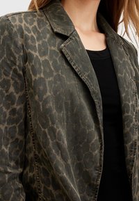 Leopardmönstrad blazer i olivgrön och beige, tillverkad av denim, med en notch-krage och en avslappnad passform med synliga sömdetaljer.
