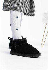 Botas de tobillo de ante negro con un acabado texturizado y un cuello suave y redondeado. Combinadas con calcetines blancos con patrones de estrellas en azul marino.