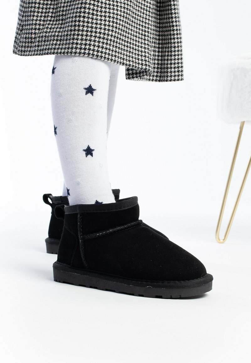 Botas de tobillo de ante negro con un acabado texturizado y un cuello suave y redondeado. Combinadas con calcetines blancos con patrones de estrellas en azul marino.