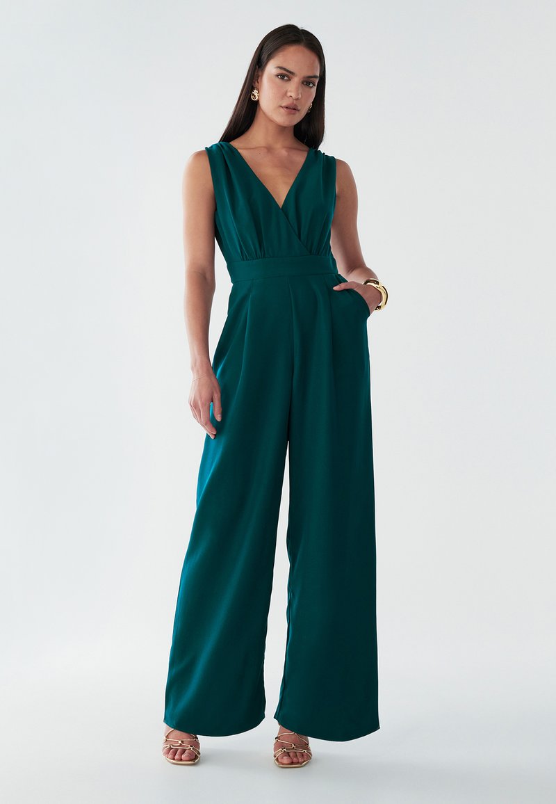 Teal ærmeløs jumpsuit med dyb V-hals, stram talje, bred ben-design og sidelommer. Glat stof med en subtil glans.