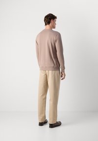 Sweatshirt beige clair à manches longues, avec des poignets côtelés et un col ras du cou, accompagné d'un pantalon beige clair et de chaussures foncées. Design simple.