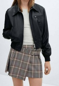 Veste bomber en simili cuir noir avec une poche zippée, associée à une mini-jupe à carreaux grise avec une ceinture et un design plissé.