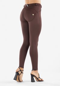 Leggings marroni con un alto punto vita, texture liscia e cuciture a contrasto. Abbinati a sandali neri con tacchi alti e cinturini incrociati.