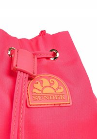 Zaino a coulisse di un vivace colore rosa brillante, con occhielli dorati lucidi e un'etichetta in gomma con un design solare. Tessuto liscio con dettagli cuciti.