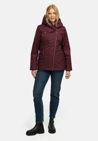 Bordowa pikowana kurtka z kapturem, zapinana z przodu na zamek, z dwoma bocznymi kieszeniami. Do tego ciemne jeansy i czarne botki za kostkę.