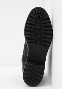 Botte noire avec tige en tissu texturé et semelle en caoutchouc épais. Le motif de la semelle comprend des rainures et des crêtes pour une meilleure adhérence. Détail de fermeture éclair sur le côté.