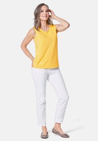 Top giallo senza maniche con scollatura rotonda, abbinato a pantaloni bianchi aderenti e décolleté grigi. Tessuto morbido con un design casual.