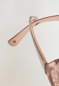 Roosa kuldne prillid, millel on peene, läbipaistev raam ja templis tähtaktsent. Kerge disain, millel on poleeritud tekstuur.