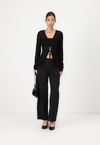 Black sheer knitted cardigan with a tie-front detail, paired with tailored black wide-leg trousers and black heels, holding a small bag.