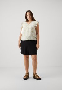 Blouse crème légèrement à motifs avec des manches froncées, associée à un short noir et des sandales marron à lanières. Tenue d'été simple et décontractée.