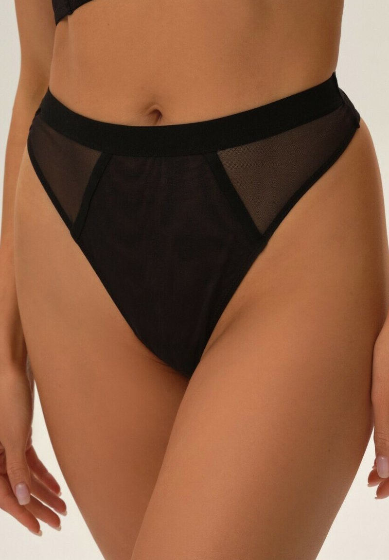 Schwarze Lingerie mit transparenten Mesh-Panels, hohem Schnitt, weichem elastischen Bund und glatter Textur. Minimalistische und figurbetonte Silhouette.