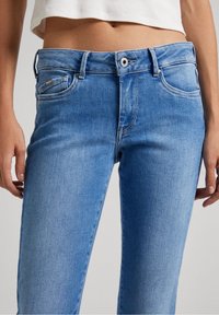 Lichtblauwe denim jeans met een getailleerde pasvorm, vijf zakken en een knoopsluiting. De stof heeft een gladde textuur en een lichte vervaging.