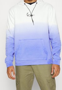 Ombre hoodie transitioning from white to light blue, featuring a front pocket, drawstring hood, and embroidered logo in black.