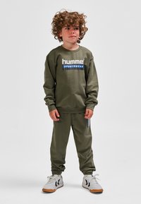 Olivengroen sweatshirt met het "hummel SPORTSWEAR" logo, gecombineerd met bijpassende joggingbroek en witte sportschoenen met zwarte accenten.