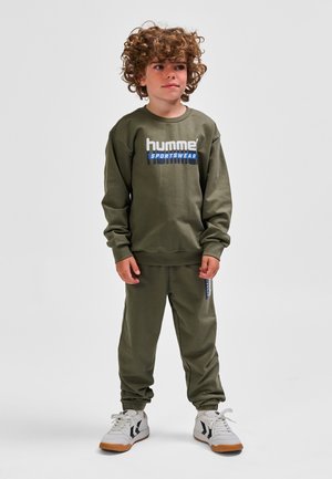 Olivgrünes Sweatshirt mit dem "hummel SPORTSWEAR"-Logo, kombiniert mit passenden Jogginghosen und weißen Sportschuhen mit schwarzen Akzenten.