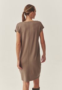 Knielanges, braunes Strickkleid mit kurzen Ärmeln, runder Ausschnitt und vertikaler Nahtdetail auf der Rückseite. Geschmeidige Textur, lässiges Design.