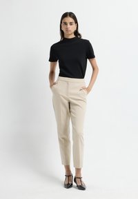 Zwarte korte mouwen top gecombineerd met beige op maat gemaakte broek met zijzakken. Het model draagt zwarte T-strap hakken. Eenvoudig, strak ontwerp.