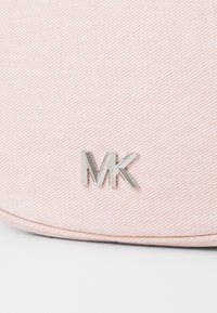 Borsa in tessuto rosa con texture, caratterizzata da un prominente logo argento "MK". Il design include motivi a coste diagonali e una forma arrotondata.