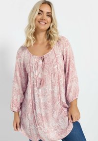 Kukallinen paita vaaleanpunaisena, jossa on valkoisia paisley-kuvioita. Ominaisuuksiin kuuluu pyöreä kaula-aukko, pitkät hihat ja edessä solmittava yksityiskohta.