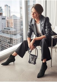 Chaqueta de moto de cuero negra sobre una blusa blanca, combinada con pantalones negros de cintura alta y botas hasta el tobillo. Accesorios con un bolso mini de estampado.