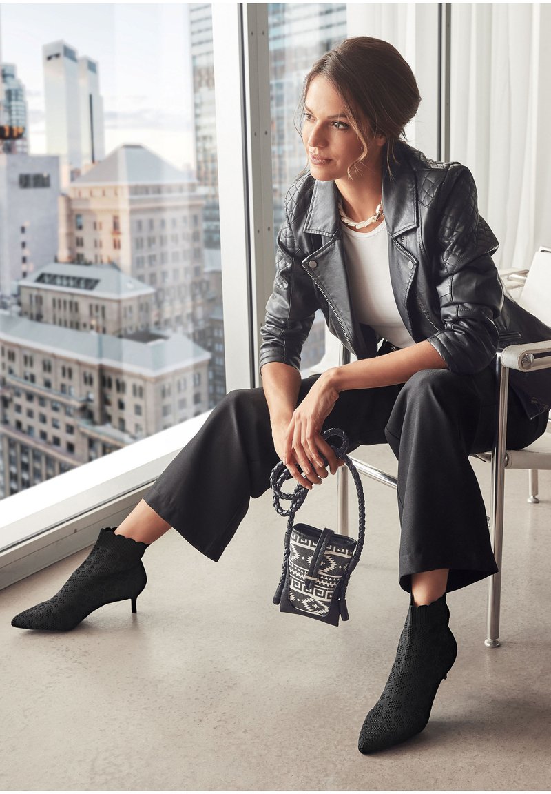 Chaqueta de moto de cuero negra sobre una blusa blanca, combinada con pantalones negros de cintura alta y botas hasta el tobillo. Accesorios con un bolso mini de estampado.