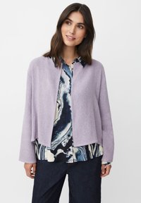 Ljust lila, strukturerad cardigan med öppen framsida och långa ärmar, lagd över en mönstrad blå och vit skjorta, i kombination med mörka jeans.