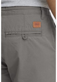 Des shorts en tissu gris dotés d'une fermeture à bouton et d'une poche arrière avec une étiquette en cuir marron portant l'inscription "BLEND". La texture semble lisse.