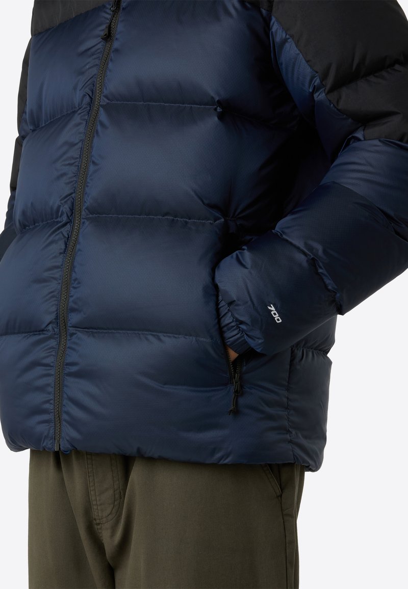Marineblaue Pufferjacke mit einem Reißverschluss, ausgestattet mit schwarzen Akzenten und einem gesteppten Design. Elastische Bündchen und seitliche Taschen runden den Look ab.