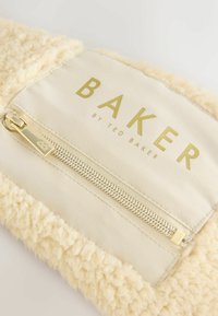 Vaaleanbeige karvatekstuuriinen pussukka, jossa on sileä vaaleanbeige kangasosio. Varustettu kultaisella vetoketjulla ja kohokuvioidulla brändinimellä "BAKER" kullalla.