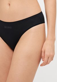 Zwarte bikini onderkant van gladde stof met een lage taille en minimale dekking; heeft subtiel zwart BORG-logo aan de voorkant.