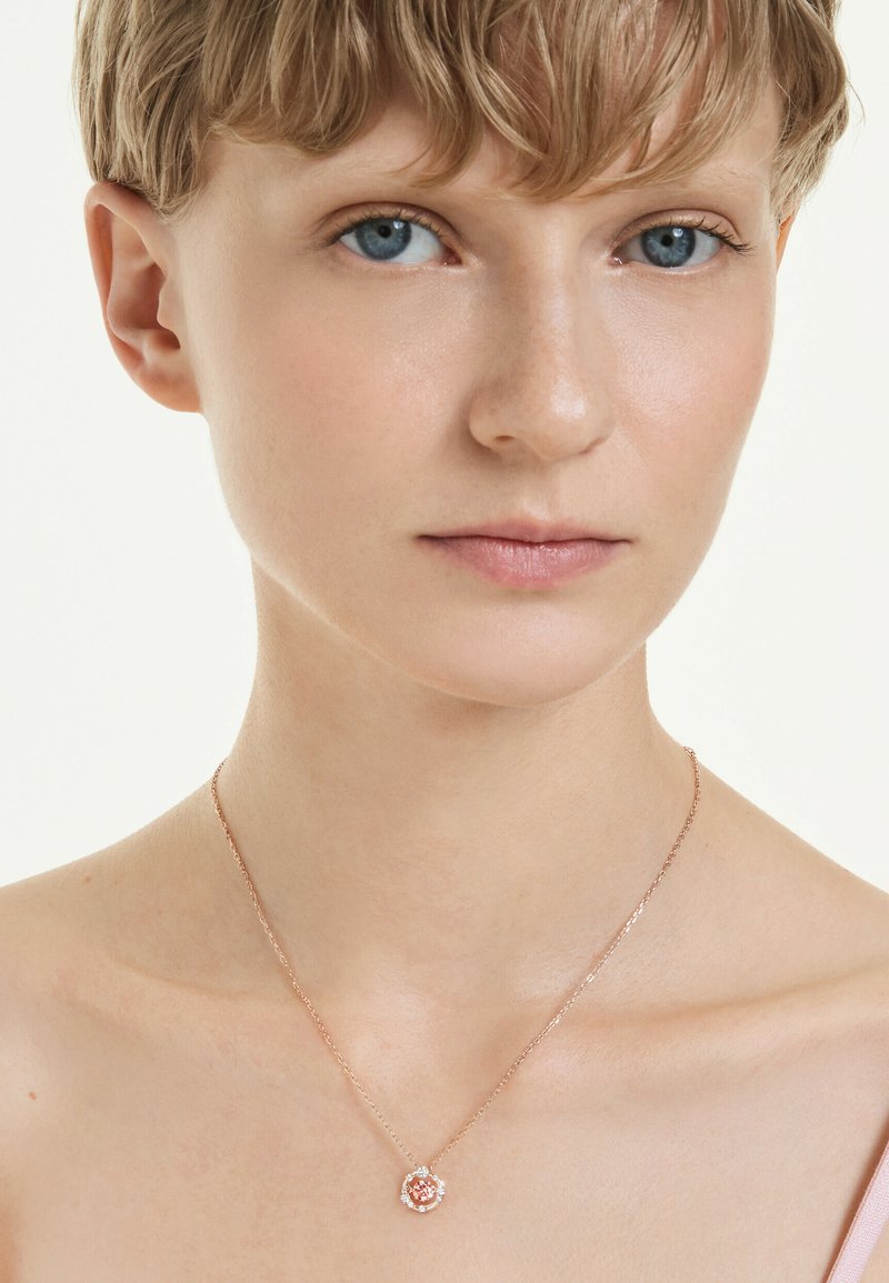 Halskette aus Roségold mit einem floralen Anhänger, der einen zentralen rosa Edelstein und kleine klare Steine zeigt, befestigt an einer filigranen Kette.