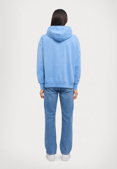 Hoodie blu chiaro con una vestibilità morbida, dotato di cappuccio con cordino, polsini e vita a coste, abbinato a jeans blu chiaro a gamba dritta.